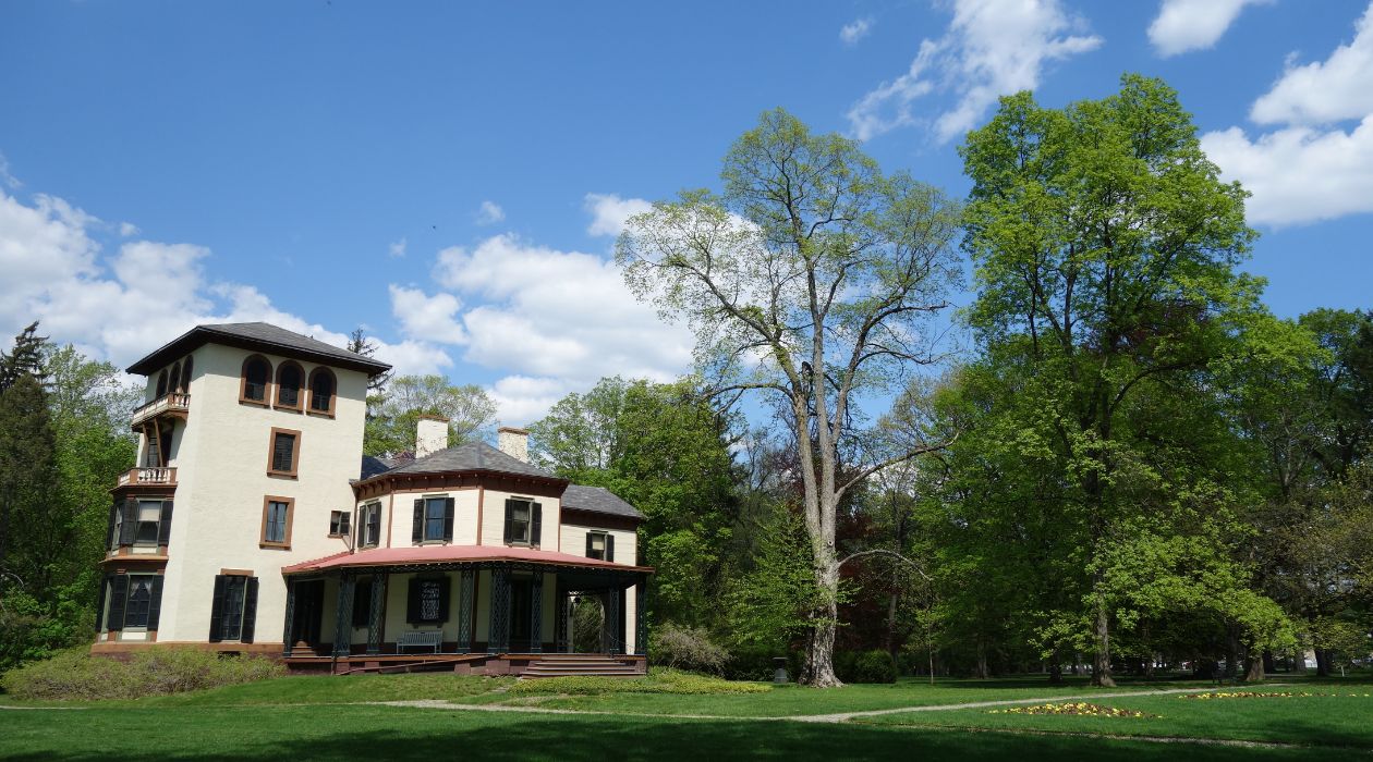 Locust Grove Estate in Poughkeepsie, an ornate white house with brown trim surrounded by trees with green leaves and a green lawn photographed on a sunny day.